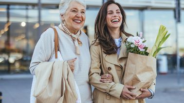 Zwei Frauen lachen und tragen Einkaufstaschen beim gemeinsamen Stadtbummel.