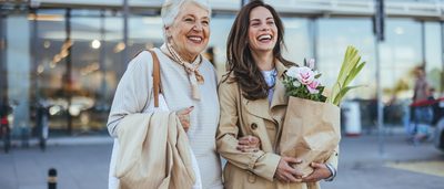 Zwei Frauen lachen und tragen Einkaufstaschen beim gemeinsamen Stadtbummel.