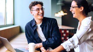 Zwei Kollegen lachen gemeinsam bei der Arbeit am Schreibtisch – entspannte Atmosphäre trotz Alltagsstress