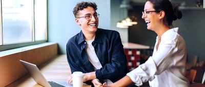 Zwei Kollegen lachen gemeinsam bei der Arbeit am Schreibtisch – entspannte Atmosphäre trotz Alltagsstress
