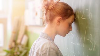 Schülerin lehnt den Kopf an die Tafel – typische Prüfungsangst und Lampenfieber vor einer Prüfung