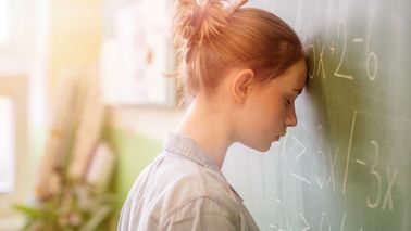 Schülerin lehnt den Kopf an die Tafel – typische Prüfungsangst und Lampenfieber vor einer Prüfung