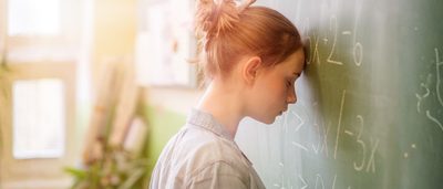 Schülerin lehnt den Kopf an die Tafel – typische Prüfungsangst und Lampenfieber vor einer Prüfung