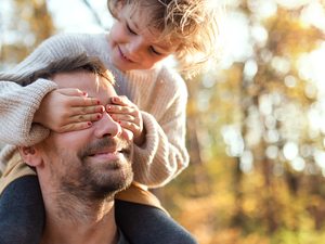Mädchen ist auf den Schultern ihres Vaters und hält ihm die Augen zu