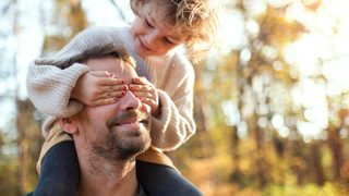 Mädchen ist auf den Schultern ihres Vaters und hält ihm die Augen zu