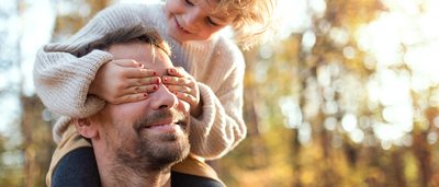 Mädchen ist auf den Schultern ihres Vaters und hält ihm die Augen zu