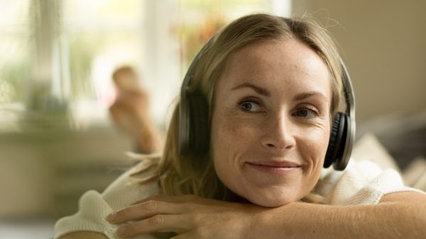 Frau liegt mit Kopfhörern auf der Couch