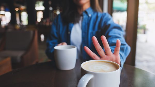 Frau schiebt bewusst eine Kaffeetasse weg