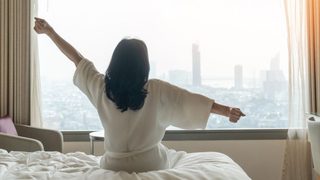 Frau sitzt morgens im Hotelbett und streckt sich nach einer Nacht im Urlaub