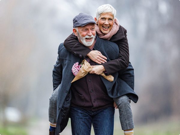 Älterer Mann trägt seine lächelnde Frau auf dem Rücken