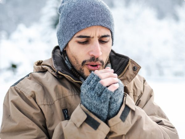 Mann mit Wintermütze und Handschuhe wärmt seine Hände