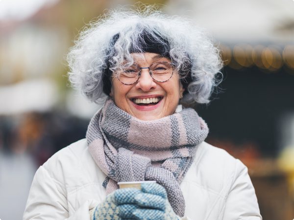 Frau mit mit einem dicken Schal, Handschuhen und einem Stirnband hält eine wärmende Tasse Tee
