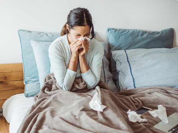 Frau sitzt im Bett und putzt sich die Nase