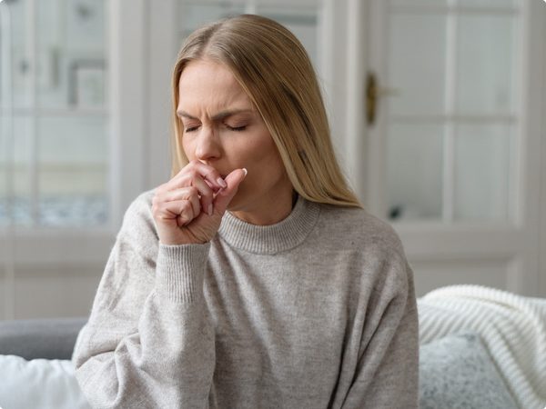 Frau sitzt zuhause und hustet sich in die Hand