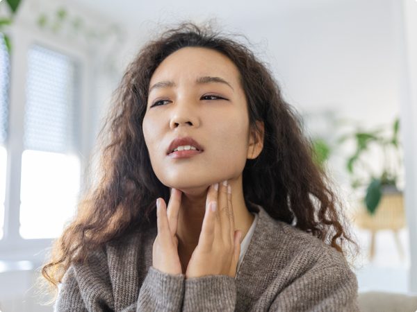 Frau tastet ihren Hals ab