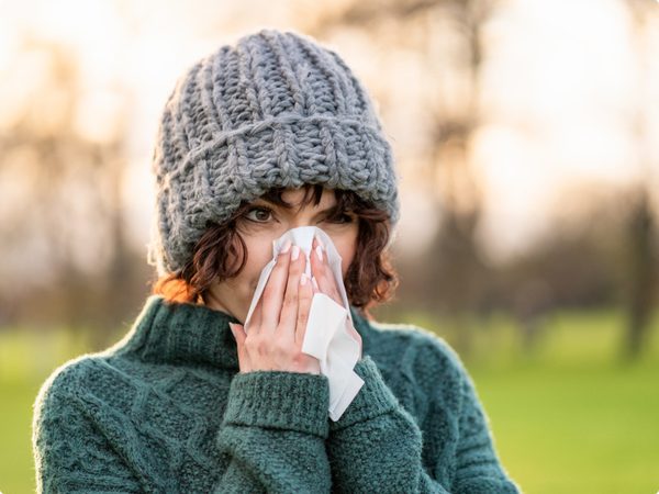 Junge Frau mit einer Strickmütze putzt sich die Nase mit einem Taschentuch