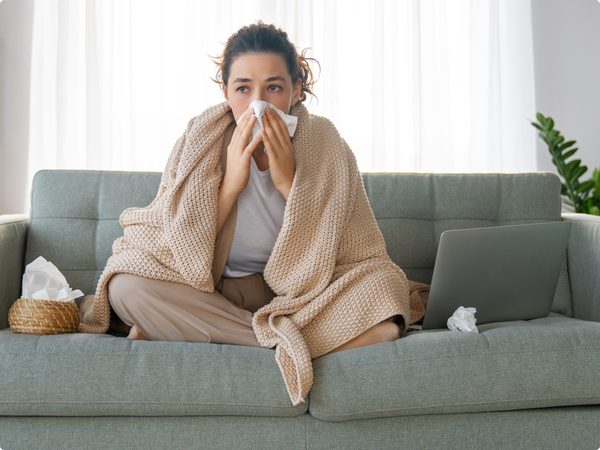 Frau sitzt auf der Couch und putzt sich die Nase