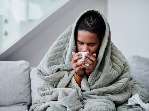 Mann in einer Decke eingekuschelt trinkt eine Tasse Tee