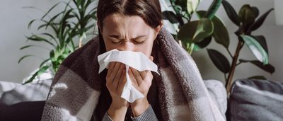 Erkältete Frau putzt sich auf Sofa die Nase.