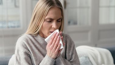 Frau niest in ein Taschentuch.