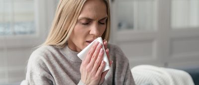 Frau niest in ein Taschentuch.