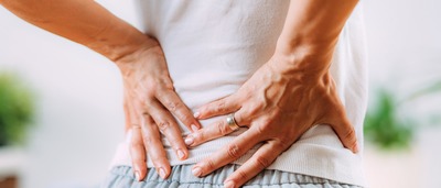 Frau hält sich wegen Rückenschmerzen an der LWS.