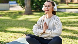 Frau mit Kopfhörern sitzt im Schneidersitz auf einer Yogamatte.