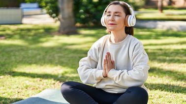 Frau mit Kopfhörern sitzt im Schneidersitz auf einer Yogamatte.