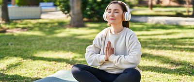 Frau mit Kopfhörern sitzt im Schneidersitz auf einer Yogamatte.