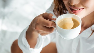 Frau trinkt im Bett eine Tasse Kaffee.