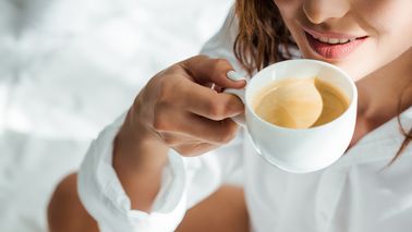 Frau trinkt im Bett eine Tasse Kaffee.