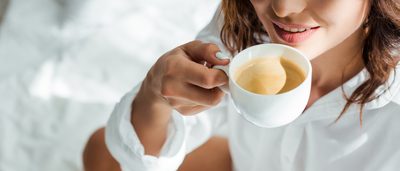 Frau trinkt im Bett eine Tasse Kaffee.