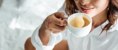 Frau trinkt im Bett eine Tasse Kaffee.