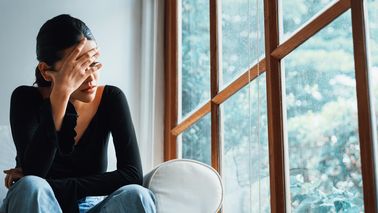 Frau sitzt auf einer weißen Couch und grübelt.