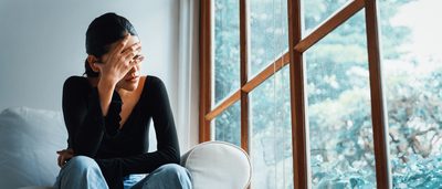 Frau sitzt auf einer weißen Couch und grübelt.