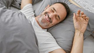 Mann liegt im Bett und wacht fröhlich auf.