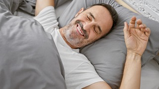 Mann liegt im Bett und wacht fröhlich auf.