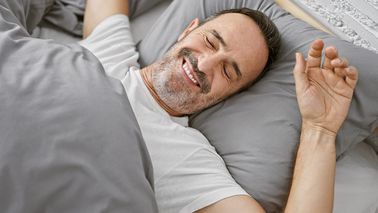 Mann liegt im Bett und wacht fröhlich auf.