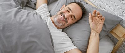 Mann liegt im Bett und wacht fröhlich auf.