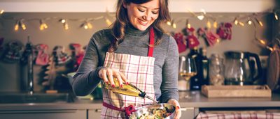 Lächelnde Frau steht in der Küche und macht einen Salat