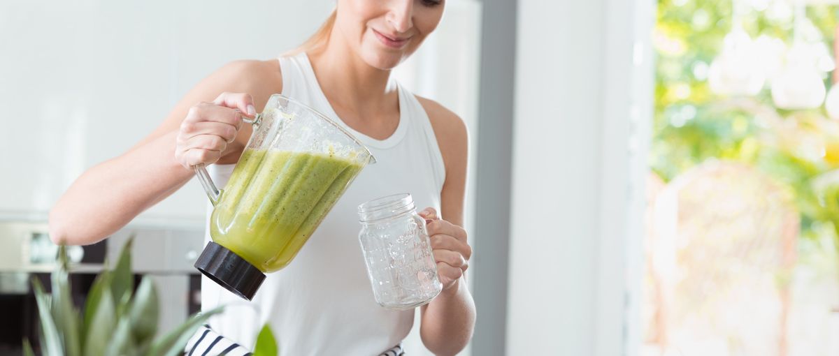 Sportliche Frau schenkt sich einen Smoothie ein.