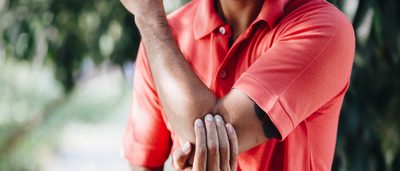 Mann mit Tennisarm oder Golferarm legt Hand auf schmerzenden Ellenbogen.