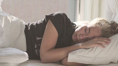 Frau schläft bei Hitze in einem Bett.