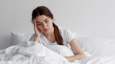 Frau, die in ihrem Bett sitzend grübelt.