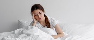 Frau, die in ihrem Bett sitzend grübelt.