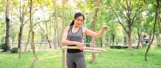 Frau macht Hula Hoop Übungen auf einer Wiese.