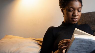 Frau sitzt abends zum Abschalten auf Couch und liest ein Buch.