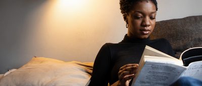 Frau sitzt abends zum Abschalten auf Couch und liest ein Buch.