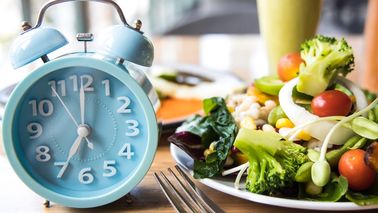 Teller mit Essen und eine Uhr als Symbol für Intervallfasten.