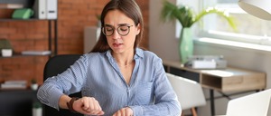 Frau bei der Arbeit, die auf ihre Armbanduhr schaut.